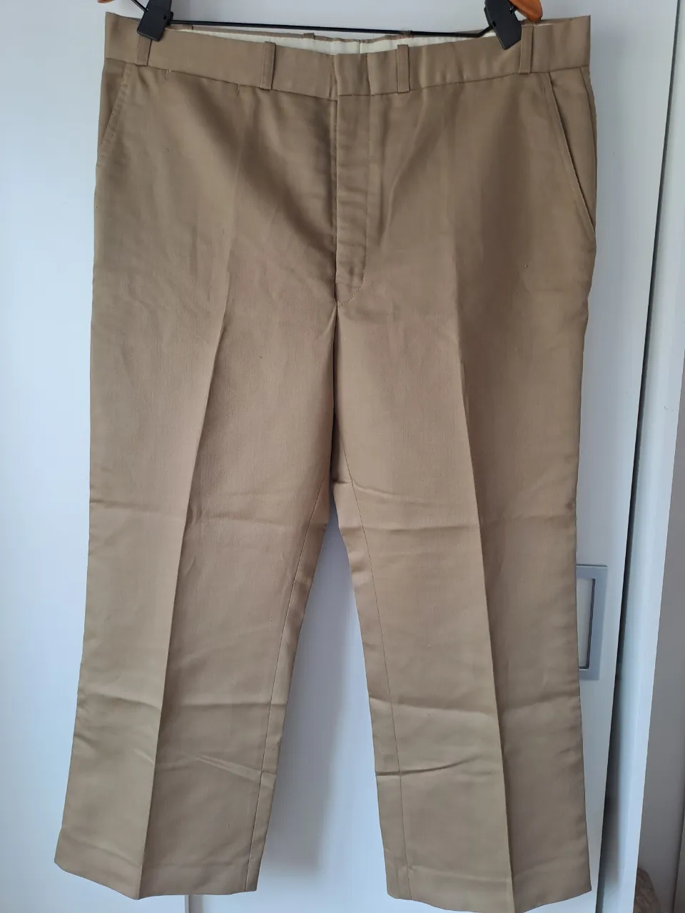 Pantalón de vestir color beige con bolsillos delanteros y traseros. Cierre y botón en la parte frontal.