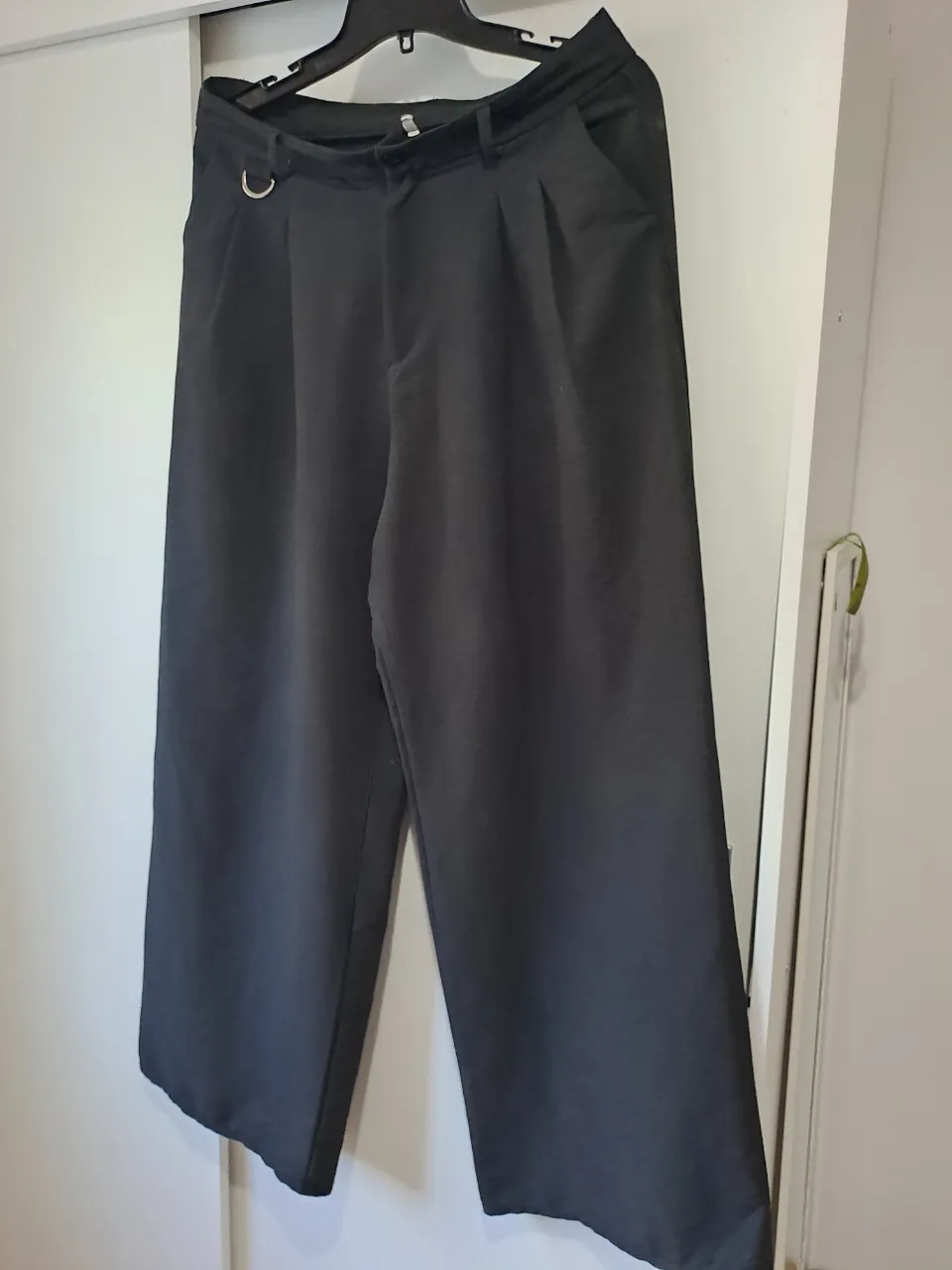 Pantalón negro con pinzas delanteras y detalle de aro metálico en la cintura.