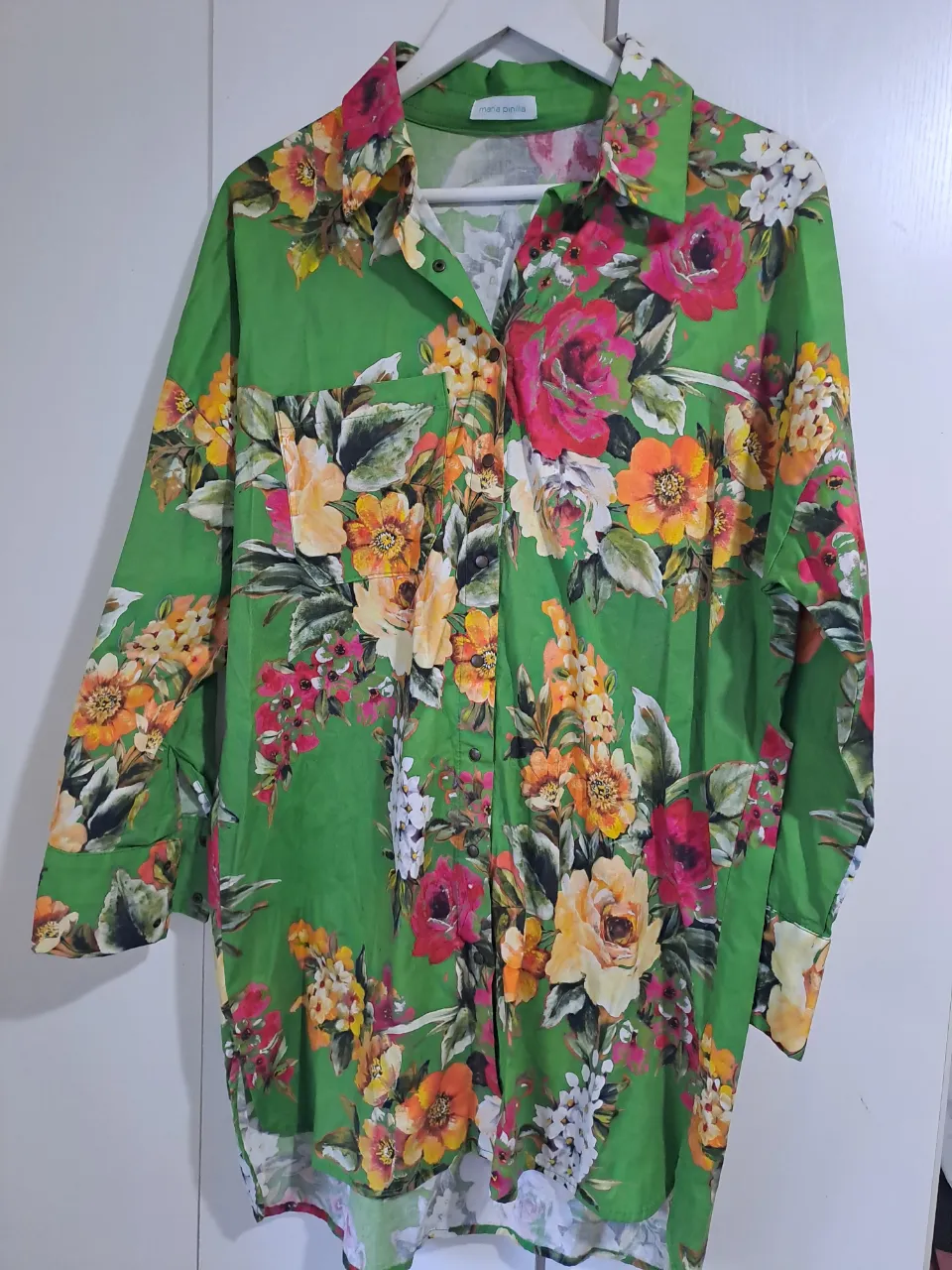 Camisa estampada con flores vibrantes en tonos verdes, rosas, naranjas y amarillos. Posee botones al frente y un bolsillo en el pecho. Ideal para un look fresco y llamativo.