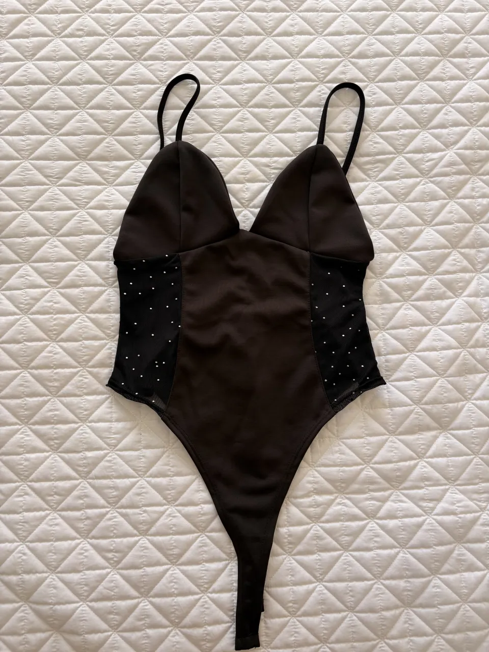 Body de color negro con tiras finas y detalles de tela con strass en los laterales. Escote pronunciado en V.