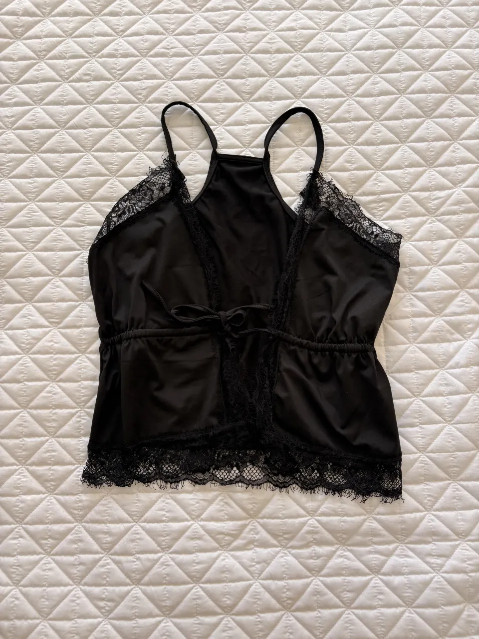 Top negro con tiras finas y detalles de encaje en los bordes. Posee un lazo para atar en la cintura.