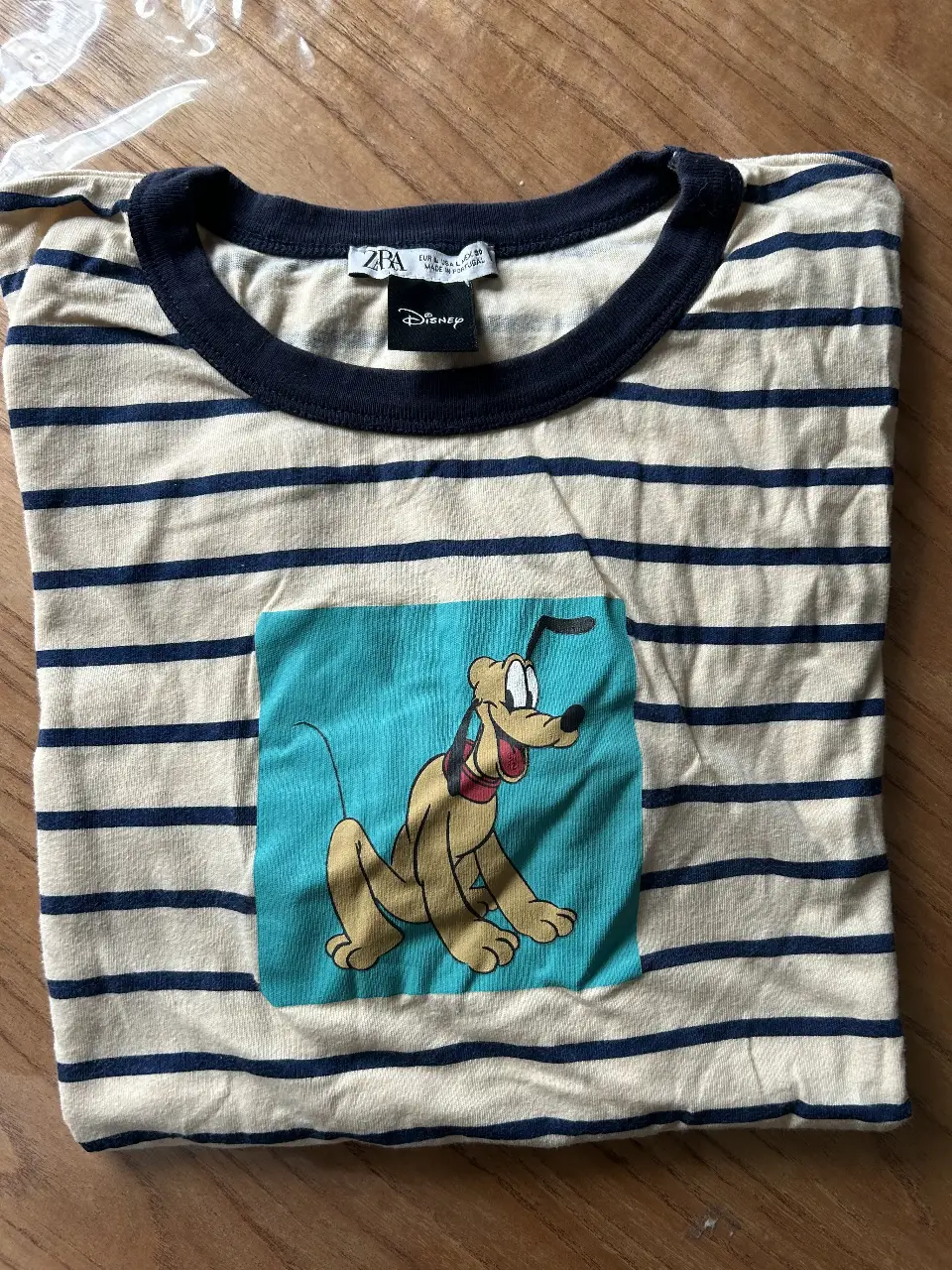 Remera de manga corta a rayas horizontales en color crema y azul marino. Cuenta con un estampado de Pluto en el frente. Ideal para un look casual y divertido.
