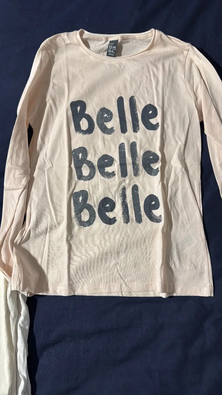 Remera manga larga de color rosa claro con estampado "Belle" en gris oscuro. Ideal para un look casual y cómodo.