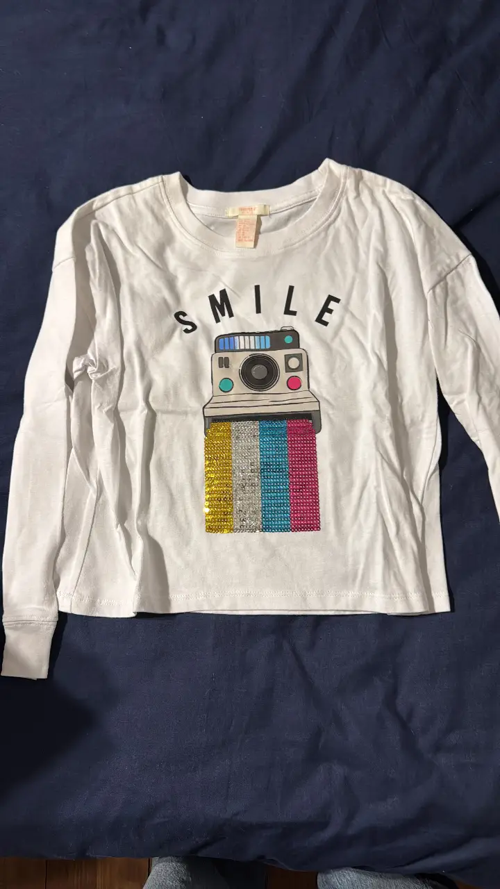 Remera manga larga blanca con estampado de cámara de fotos con detalles de lentejuelas. Diseño "SMILE". Ideal para un look casual y divertido. NUEVA