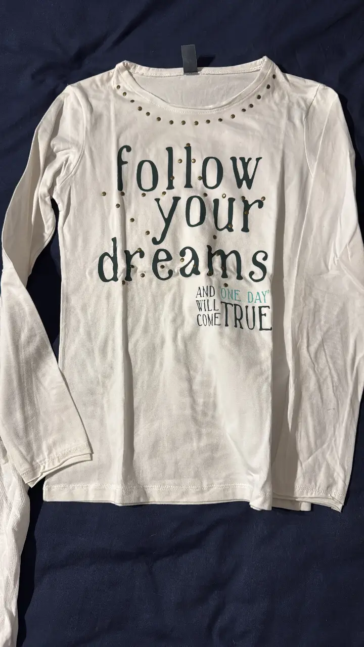 Remera manga larga blanca con la frase 'follow your dreams' estampada en negro y detalles dorados. Ideal para un look casual y con un toque inspirador.
