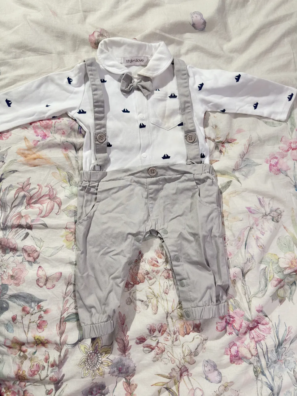 Conjunto Body que se compone de camisa manga larga con estampa de barquitos y pantalón corto con tiradores. Incluye moño.