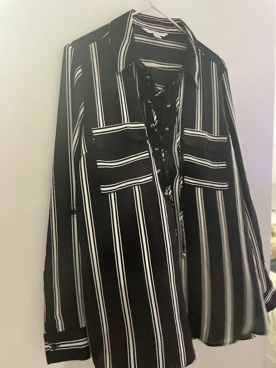 Camisa a rayas verticales en blanco y negro, con detalle de lazada en el frente. Posee dos bolsillos delanteros y mangas largas. Ideal para un look casual o de trabajo.