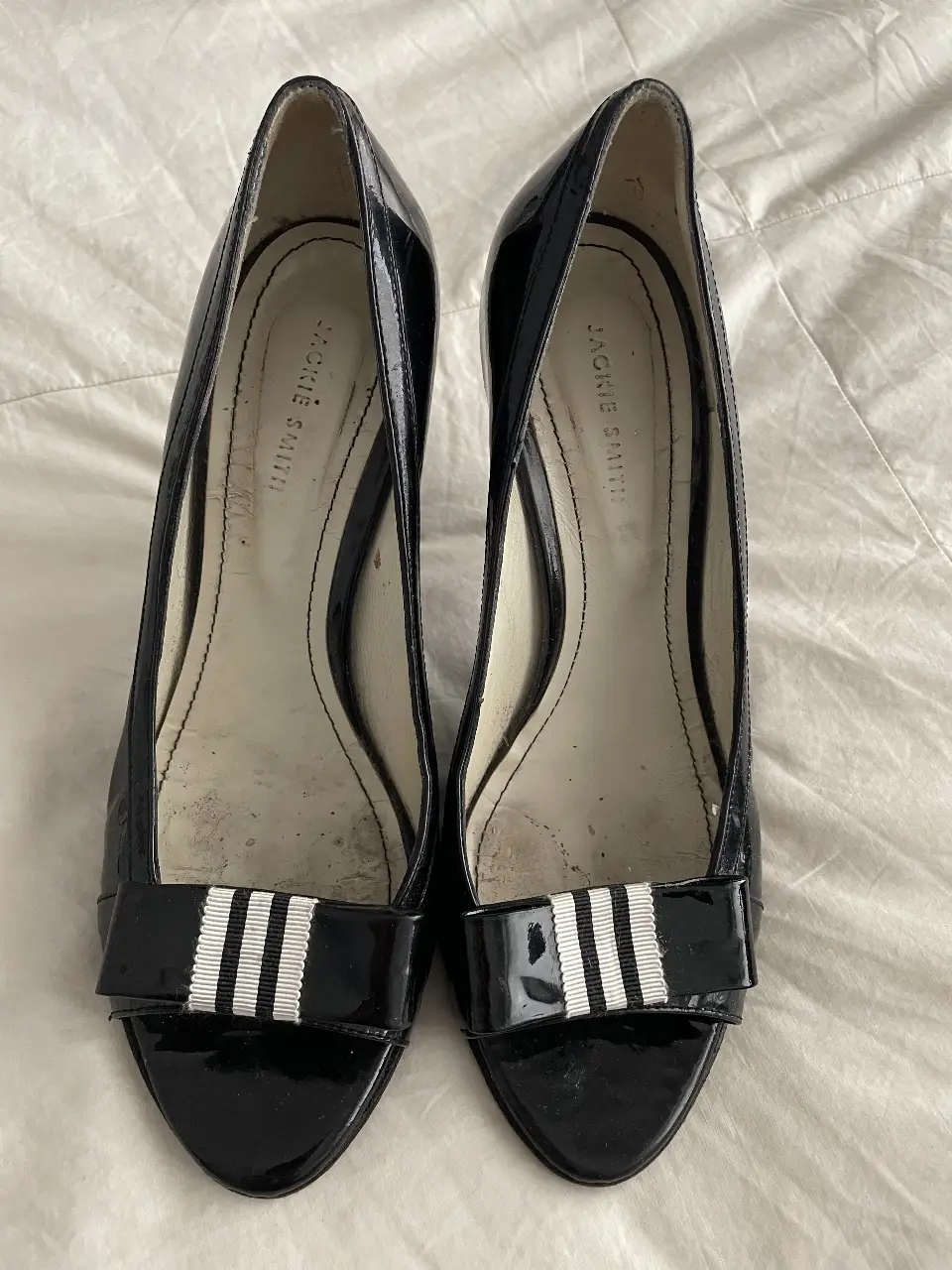 Elegantes tacos Jackie Smith de charol negro con detalle de cinta blanca y negra en la punta. Ideales para fiestas y eventos formales.