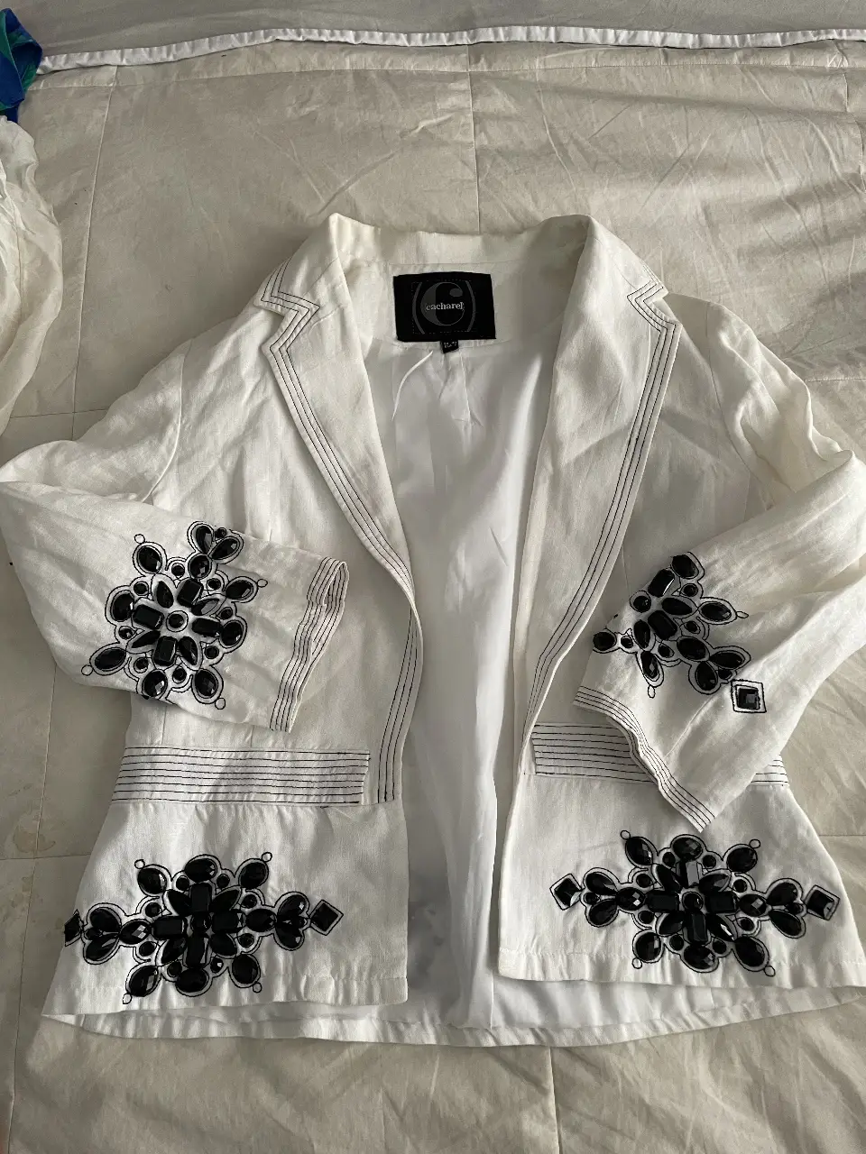 Elegante blazer blanco de la marca Cacharel, con detalles de pedrería negra en solapas, mangas y parte inferior. Ideal para un look sofisticado y con estilo.