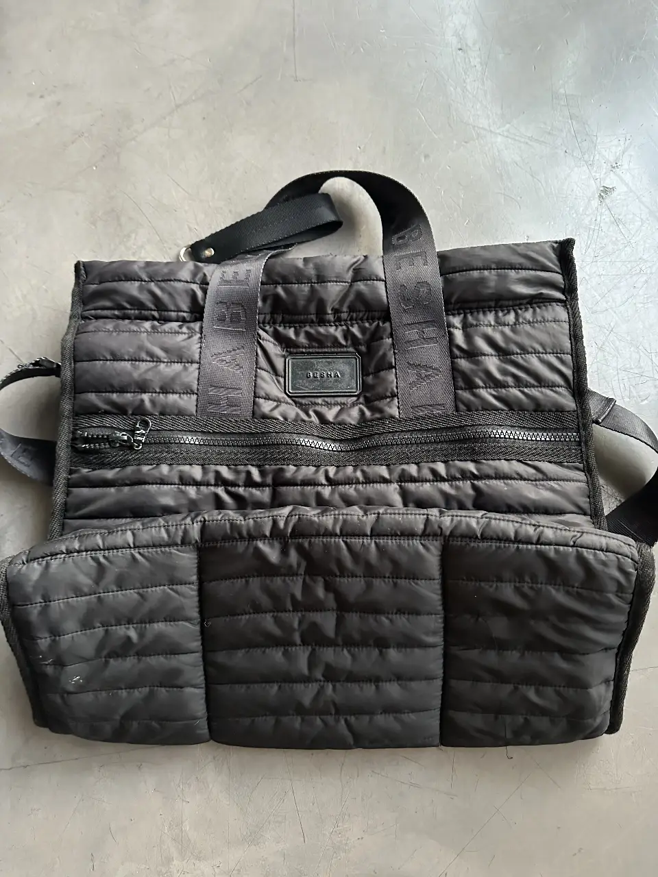 Bolso negro de Besha acolchado con correa ajustable y manijas superiores. Ideal para llevar todo lo necesario con estilo y comodidad.