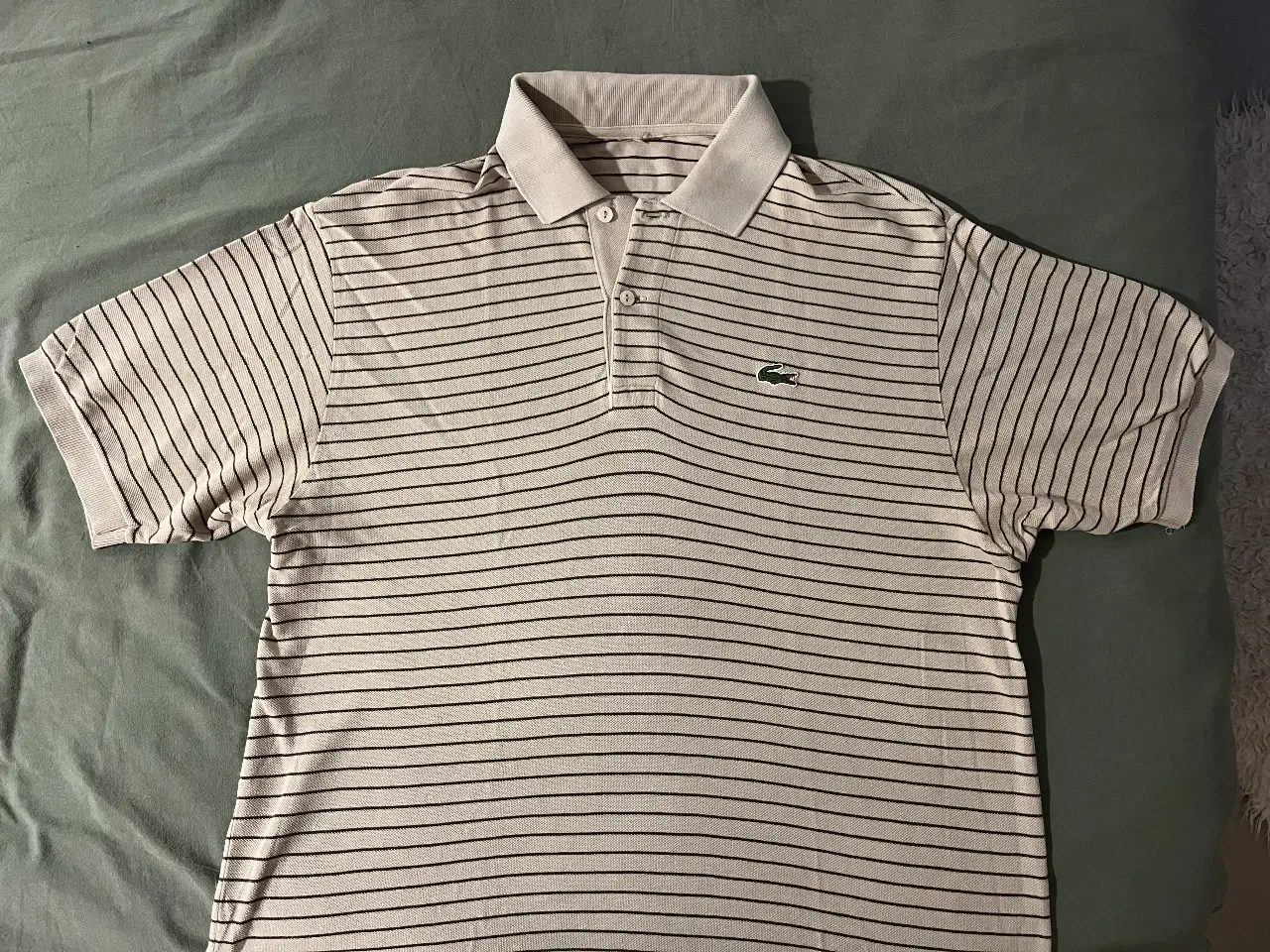 Remera polo Lacoste a rayas, de algodón, con el clásico logo del cocodrilo bordado. Ideal para un look casual y elegante.