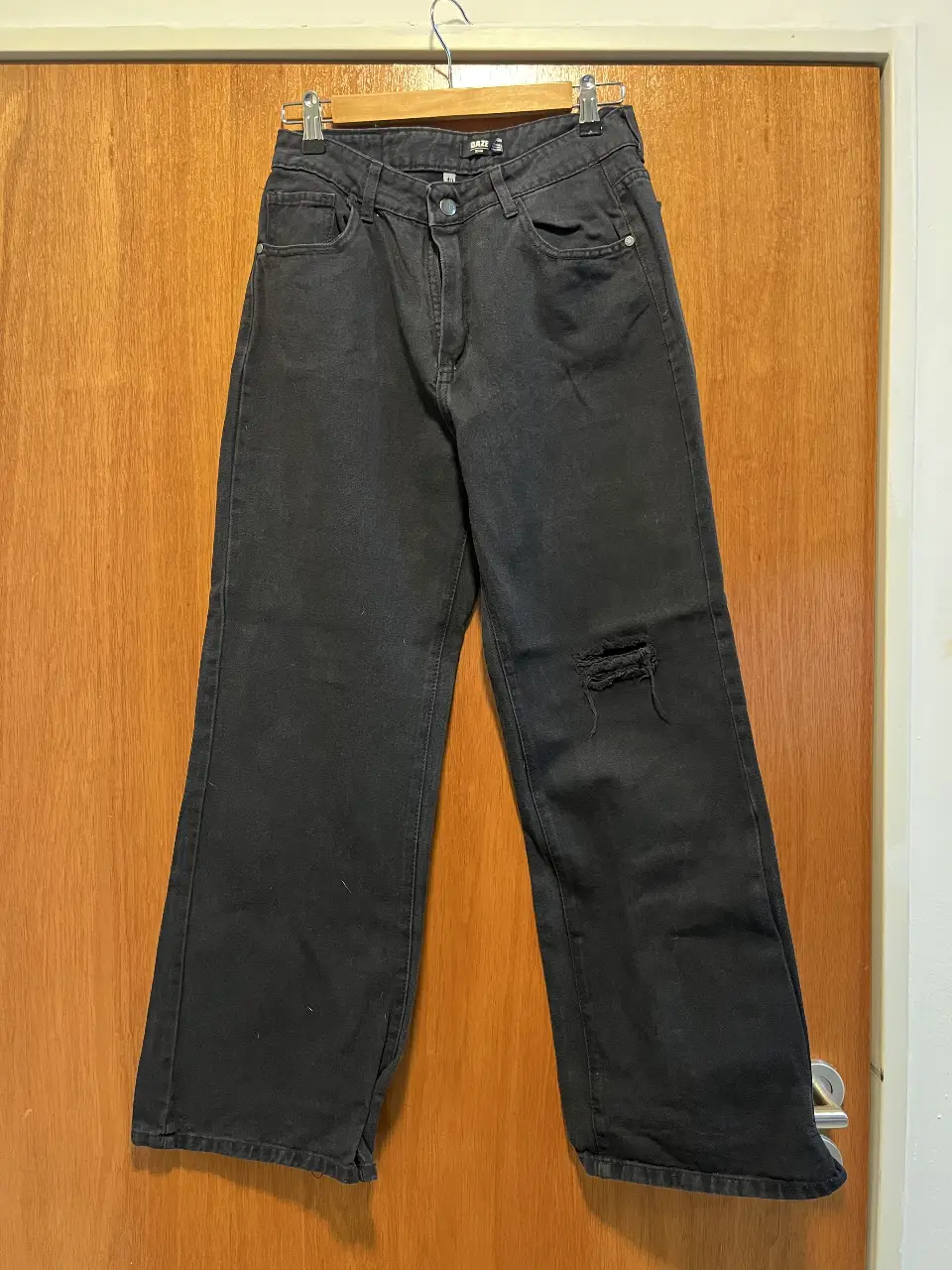 Jeans negro de corte recto con roturas en la rodilla. Tiro medio-alto, ideal para un look casual y moderno. Perfecto para combinar con remeras, camisas o sweaters.
