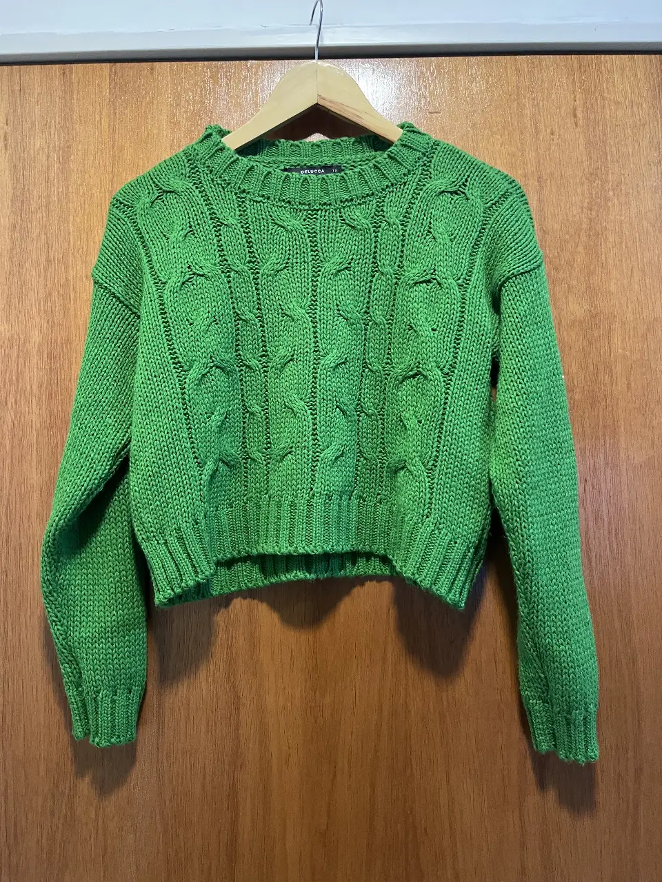 Sweater tejido de color verde, con diseño de trenzas en el frente. Cuello redondo y mangas largas. Ideal para un look casual y abrigado.