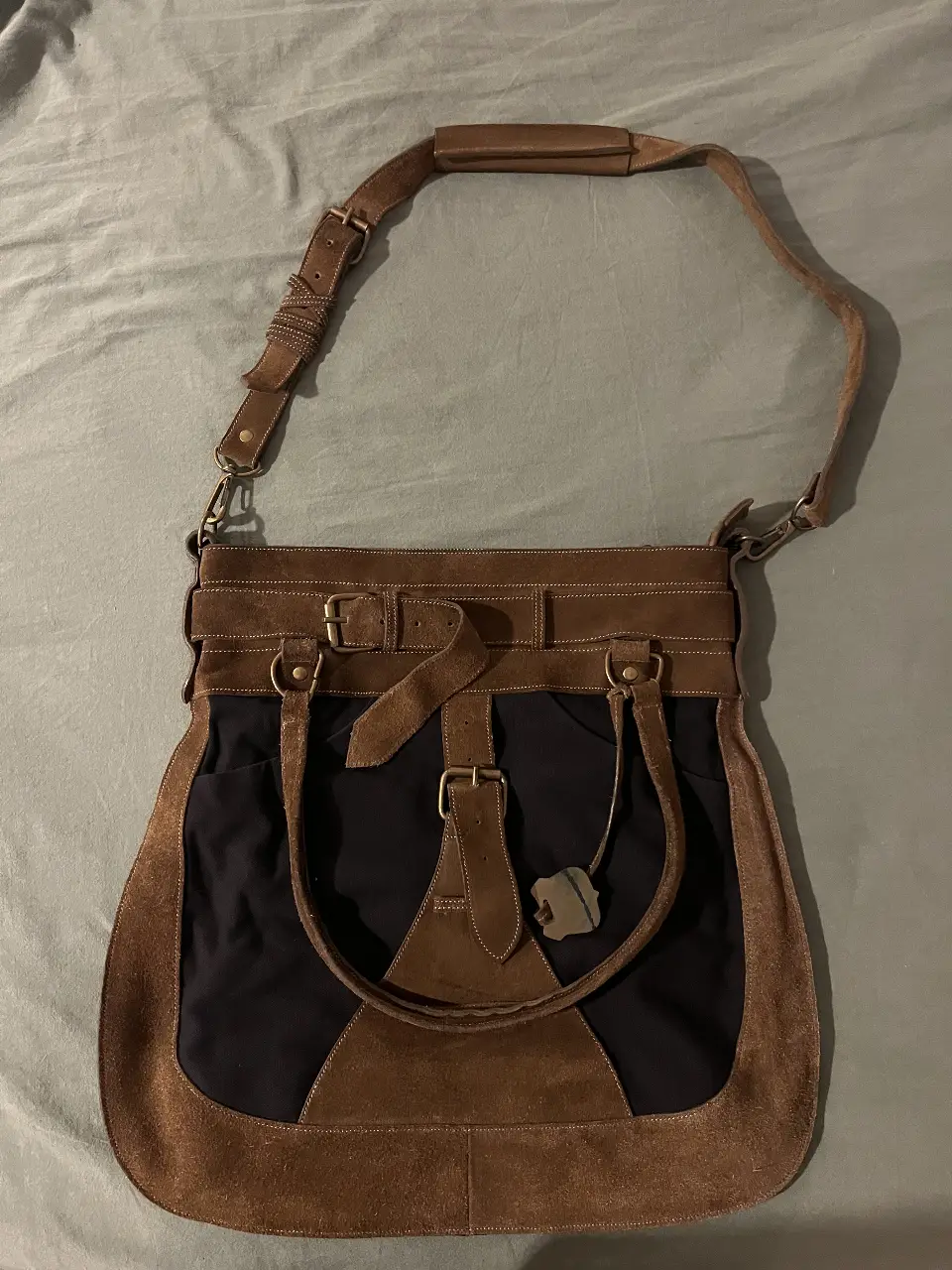 Bolso de hombro de cuero y gamuza marrón y negro, con detalles de hebillas y correa ajustable. Ideal para llevar tus pertenencias con estilo y funcionalidad.