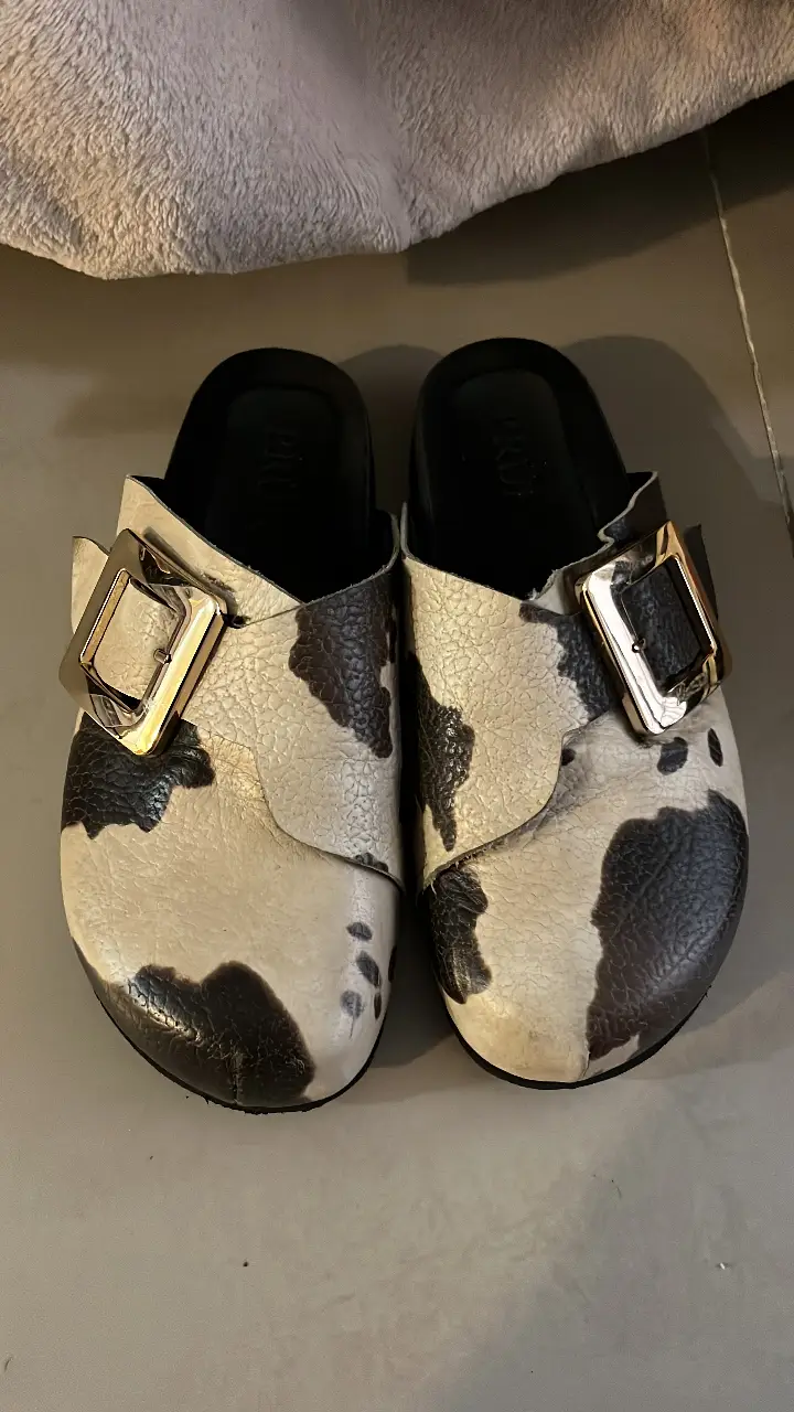 Zuecos de cuero PRUNE con estampado de vaca, hebilla dorada y suela negra. Ideales para un look casual y canchero.