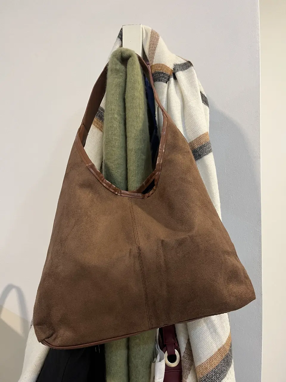 Cartera tipo hobo de gamuza marrón con manija de cuero. Ideal para un look casual y cómodo.
