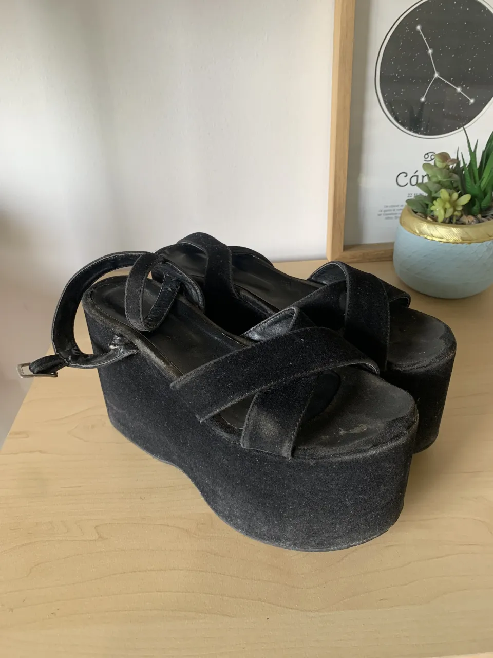 Sandalias negras gamuza, con plataforma y tiras cruzadas en el empeine. Tienen una tira fina con hebilla en el tobillo. Un poco desgastadas por el uso, le faltaría una buena limpieza de gamuza y quedan en buen estado. 