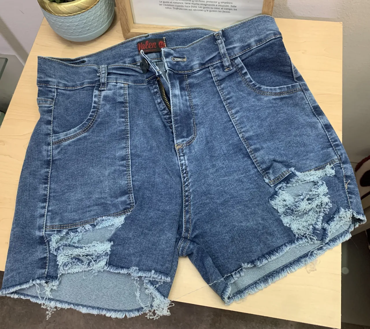 Shorts de jean azul con roturas y detalles deshilachados en los bolsillos delanteros y en el ruedo. Cierre con botón y cierre. Talle 44