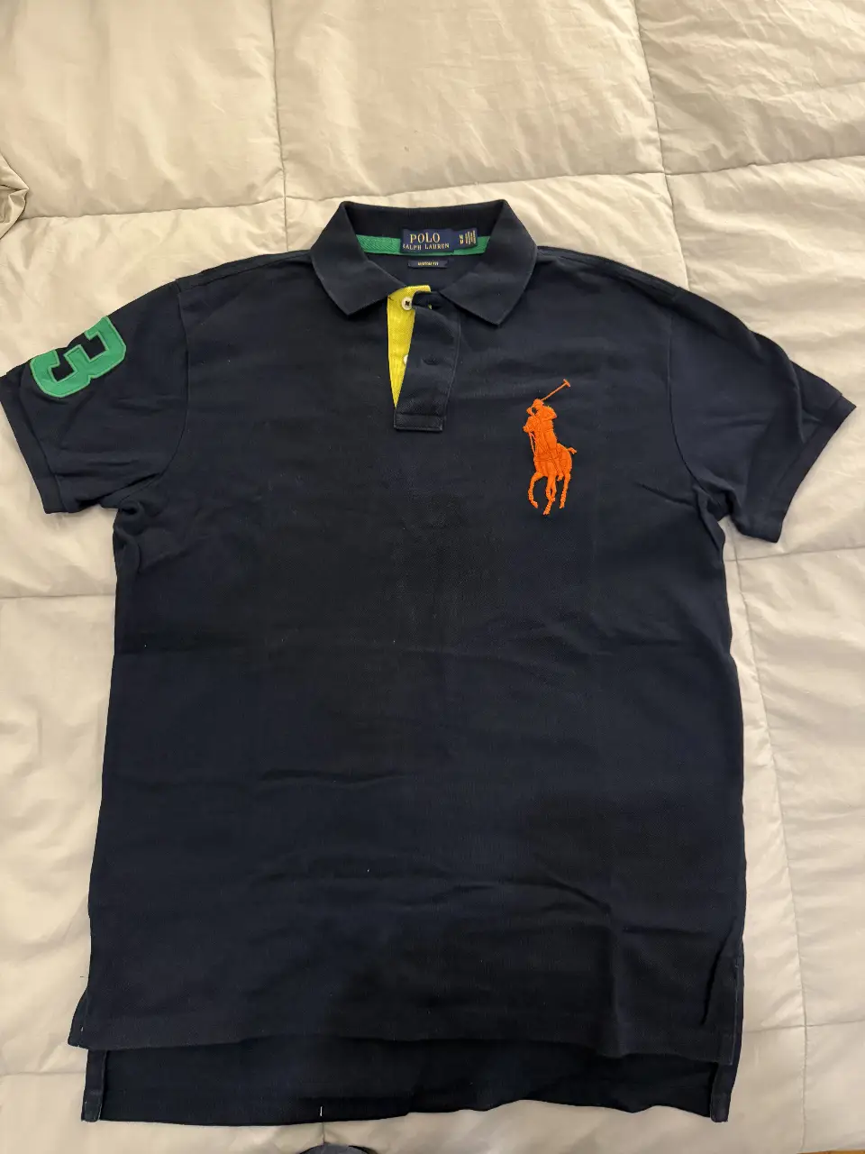 Chomba de Polo Ralph Lauren de hombre, azul marino con detalles en amarillo y verde. Logo de la marca en naranja. Corte custom fit, ideal para un look casual y canchero.