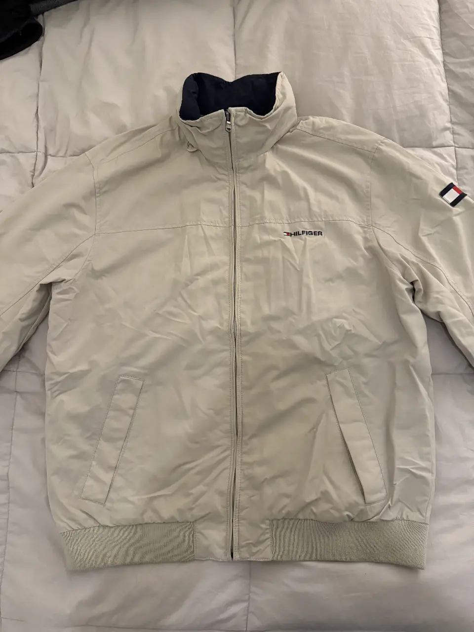 Campera bomber Tommy Hilfiger beige para hombre. Resistente a lluvia, con capucha. Con cierre frontal, cuello alto y logo de la marca en el pecho y manga. Ideal para un look casual y abrigado. Ideal para dia con lluvia.