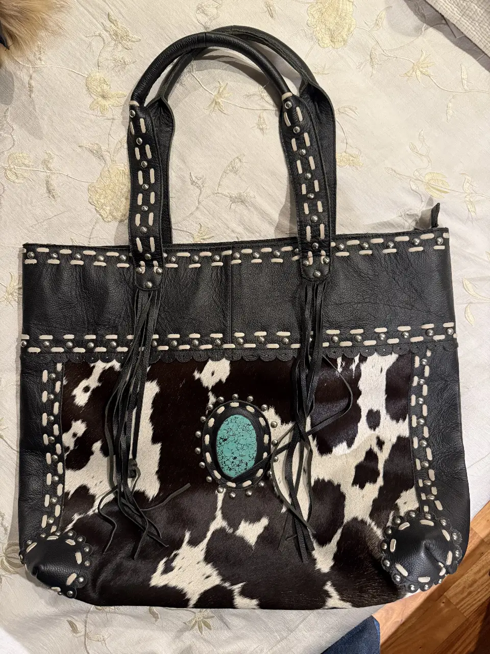 Bolso tote de cuero negro con detalles artesanales y aplique de cuero con diseño de vaca. Ideal para un look bohemio y con estilo.
