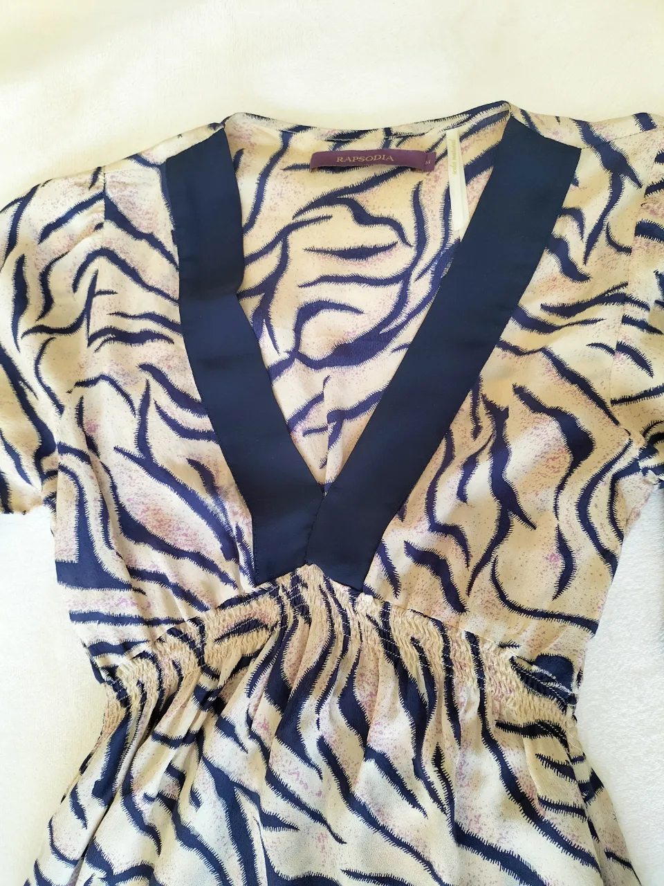 Vestido estampado animal print, con escote en V y detalles de lazo en las mangas. Largo total 90 cm. Ancho hombro 37cm. Manga abuchonada. Elástico tipo nido de abeja bajo el busto. Seda. Liviano.  Ideal para un look canchero y moderno.