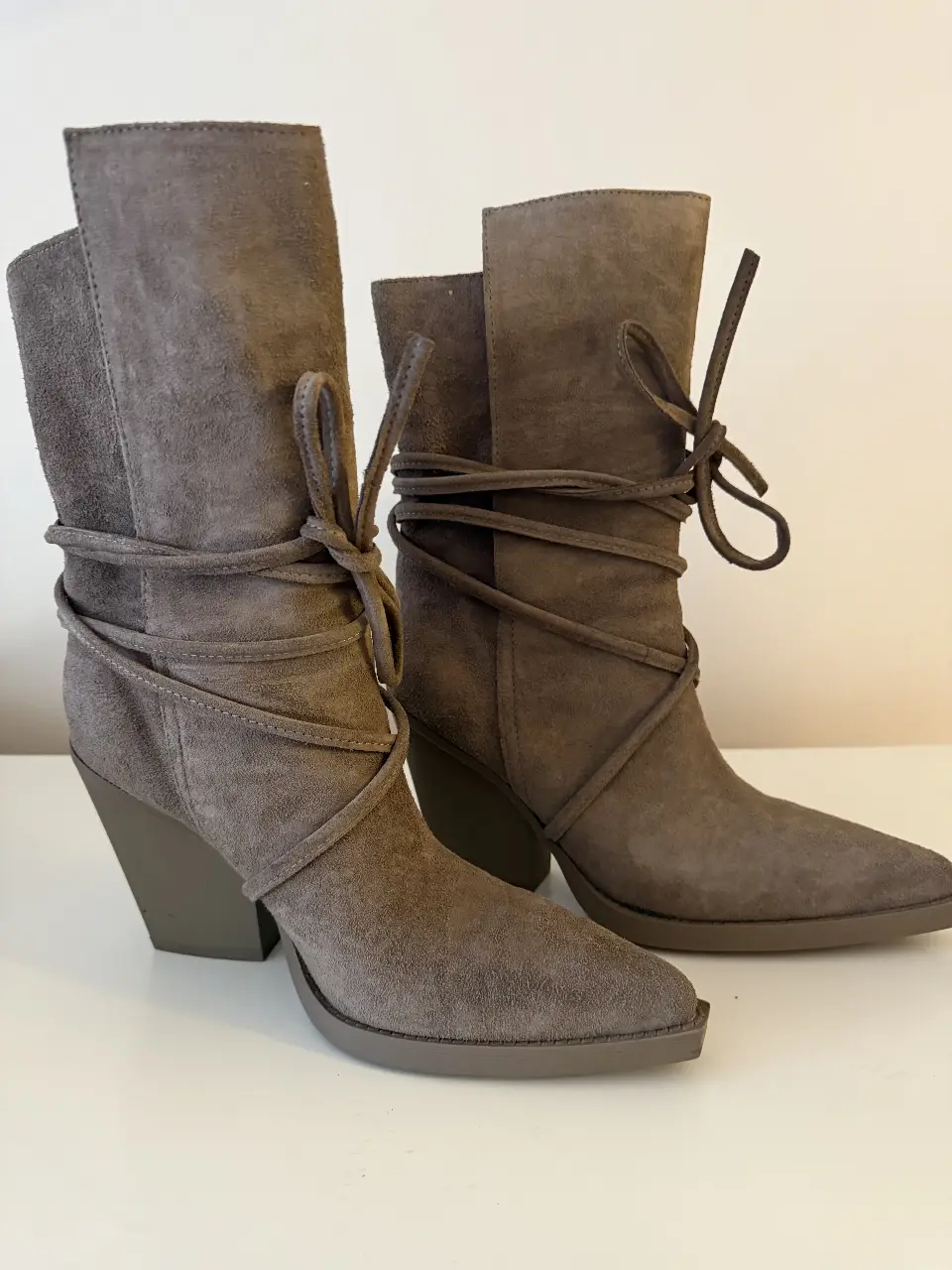 Botas de caña alta de gamuza gris taupe, con detalles de cordones y taco geométrico. Perfectas para un look moderno y sofisticado.