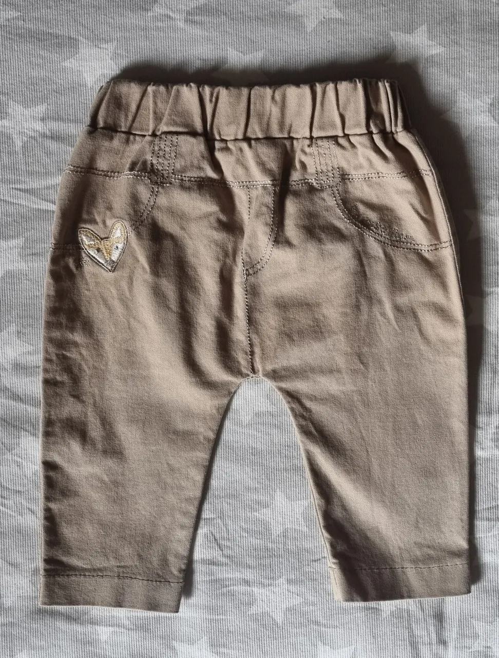 Pantalón de bebé color beige, con cintura elastizada y detalle de un zorrito en forma de corazón bordado en el bolsillo lateral. Ideal para el día a día.