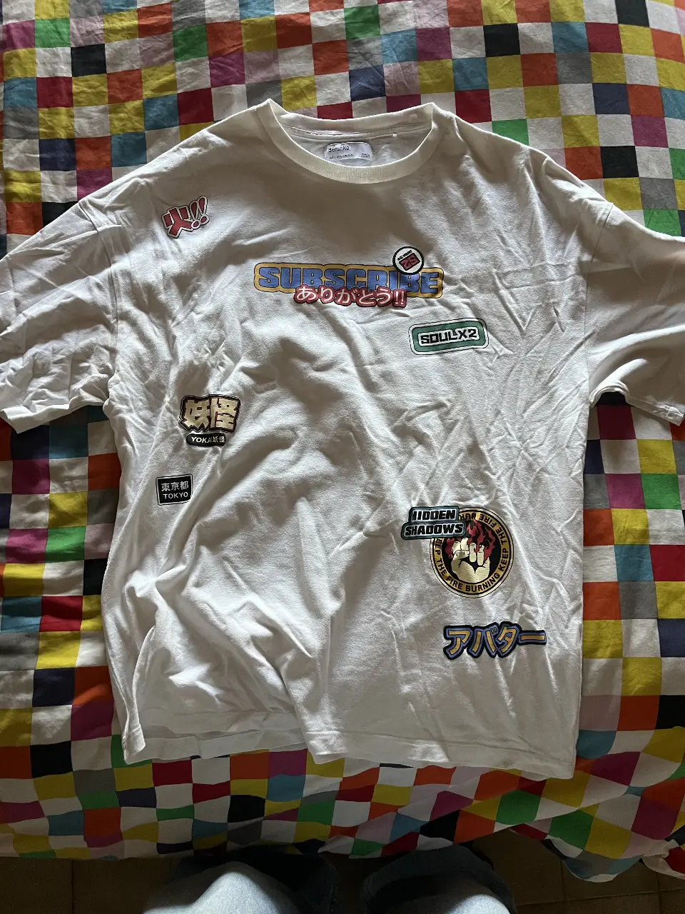 Remera blanca de manga corta con estampados de estilo anime y japonés. Diseño con múltiples parches y estampas en la parte delantera y trasera, ideal para un look streetwear.
