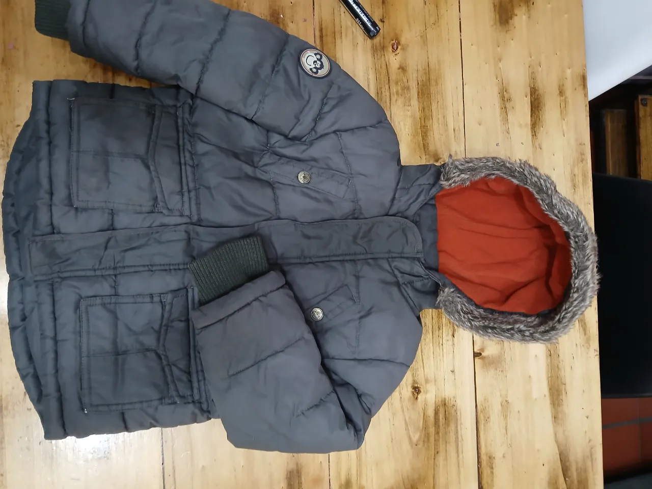 Campera de abrigo para niño, color gris con capucha forrada en naranja y detalles en verde oscuro. Ideal para el invierno.