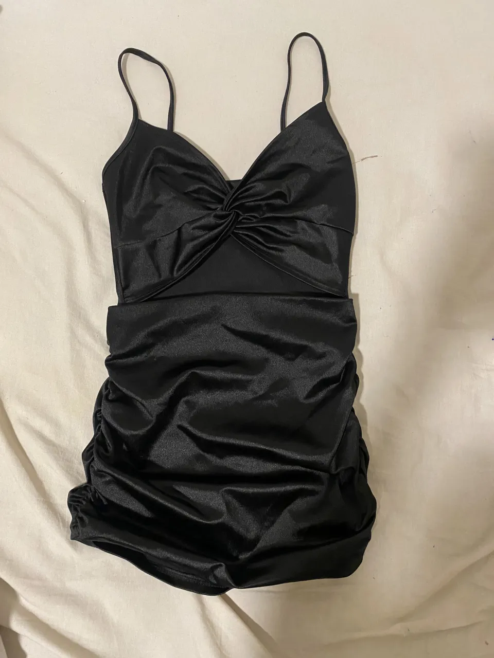 Vestido negro corto con tiras finas, escote cruzado y recorte en el abdomen. Posee fruncido en la parte inferior.
