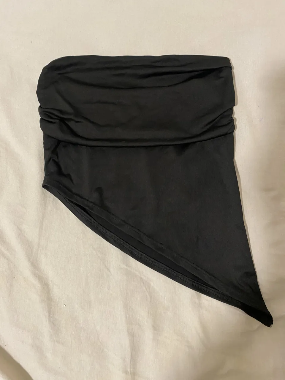 Top negro strapless con fruncido en la parte superior y corte asimétrico en la parte inferior.