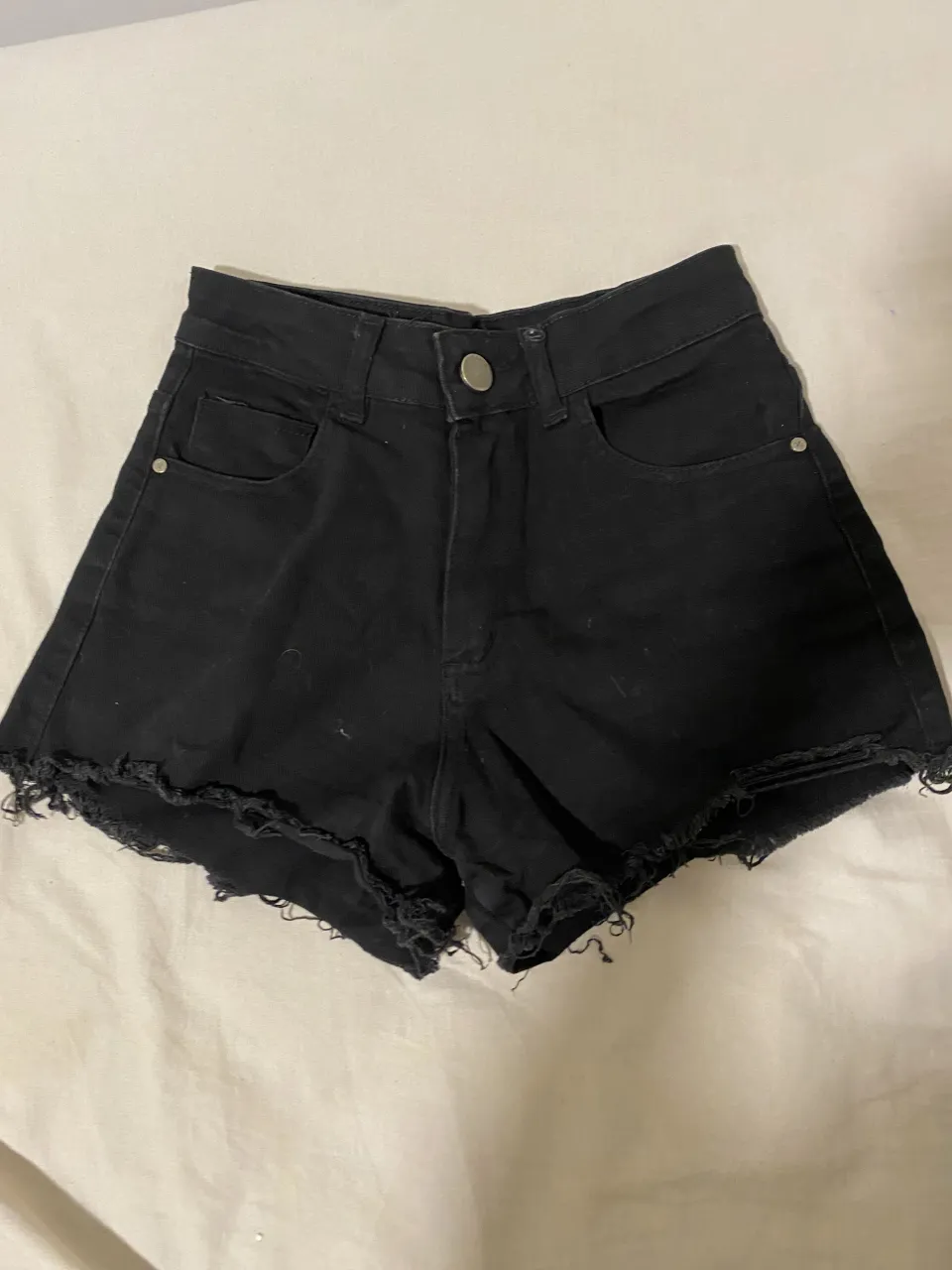 Shorts de jean negros con roturas y deshilachados en el borde inferior.