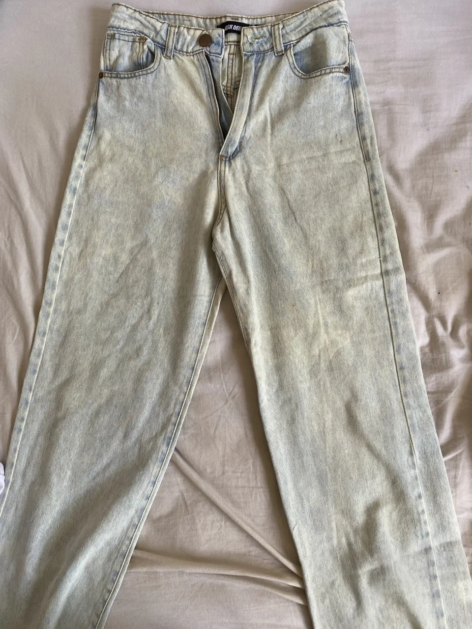 Jeans de tiro alto con lavado claro y detalles desgastados. Cierre y botón.