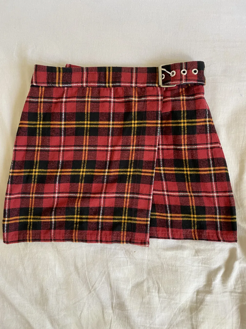 Pollera a cuadros escoceses en rojo, negro y amarillo. Tiene un cinturón con hebilla plateada y ojales.