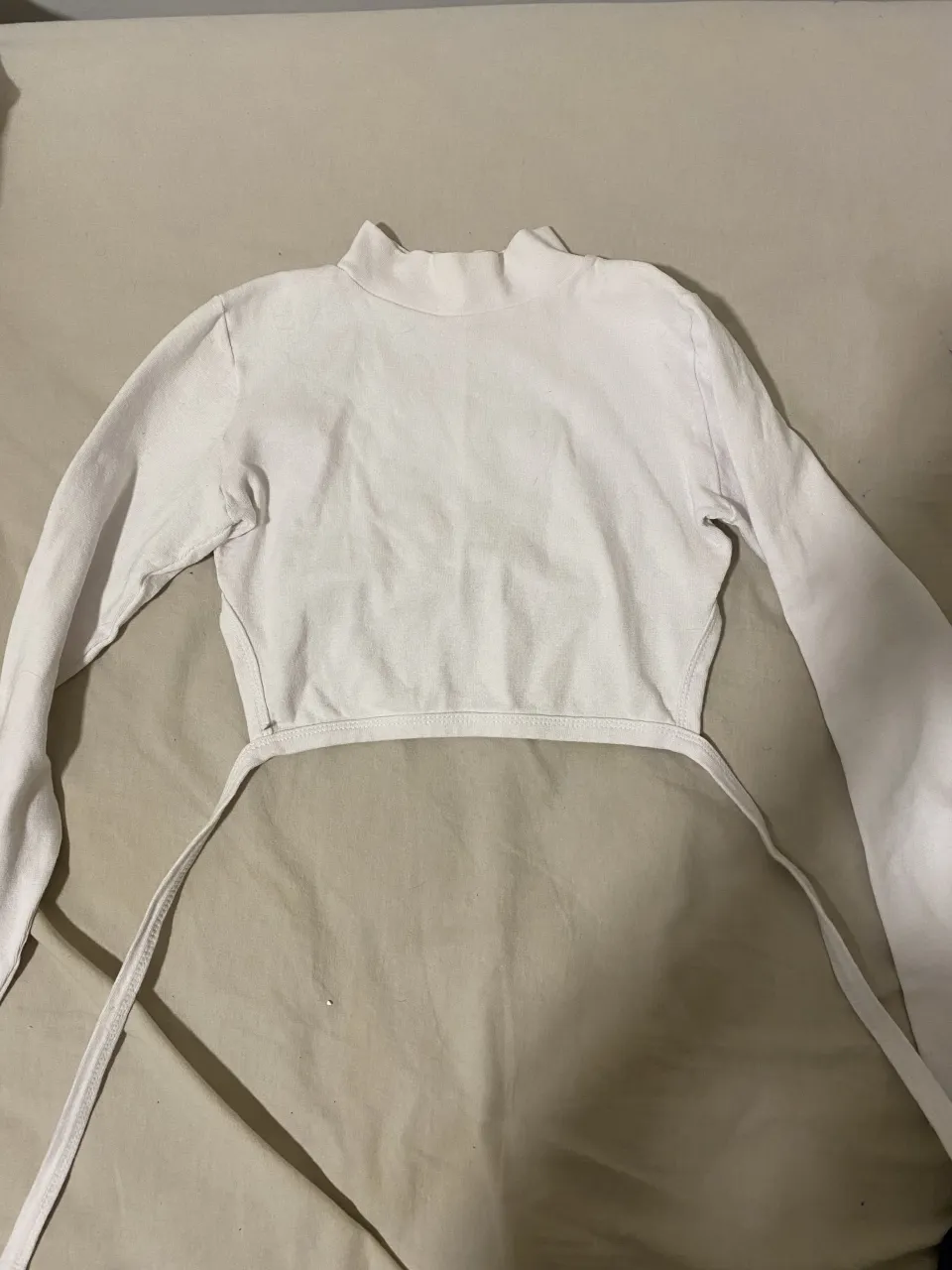 Remera blanca manga larga con cuello alto y lazos para atar en la espalda.