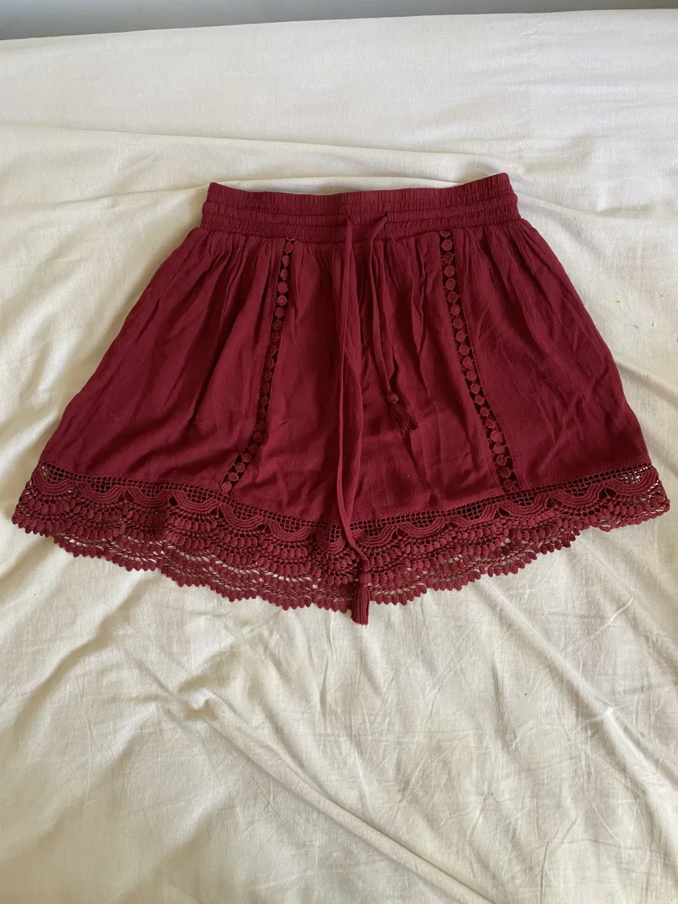 pollera de color bordo con cintura elastizada y cordón para ajustar. Posee detalles de puntilla en el ruedo y recortes con botones en los laterales.