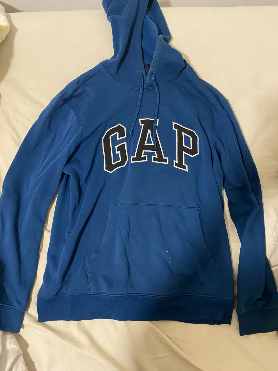 Buzo azul con capucha y cordones. Estampa grande de la marca "GAP" en el frente. Posee bolsillo tipo canguro.