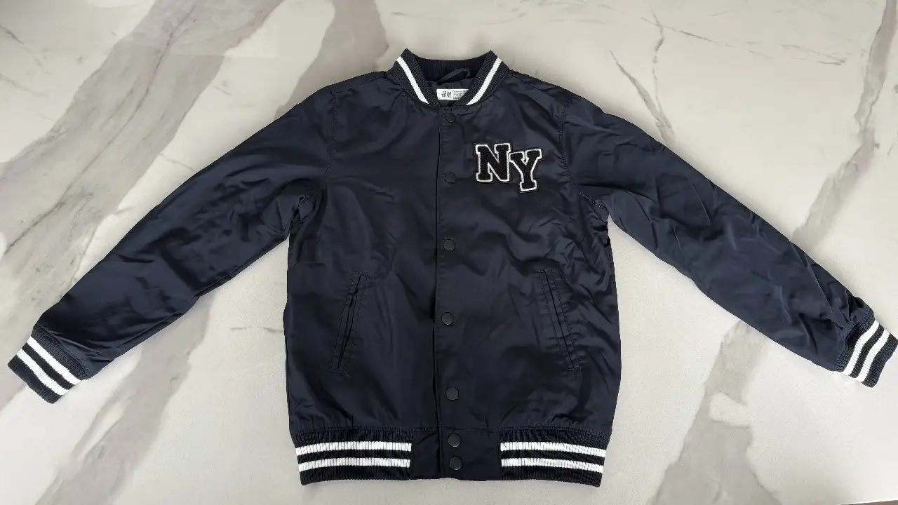 Campera bomber azul marino de H&M para niño con detalles en blanco. Presenta el logo 'NY' en el pecho. Ideal para un look casual y moderno.