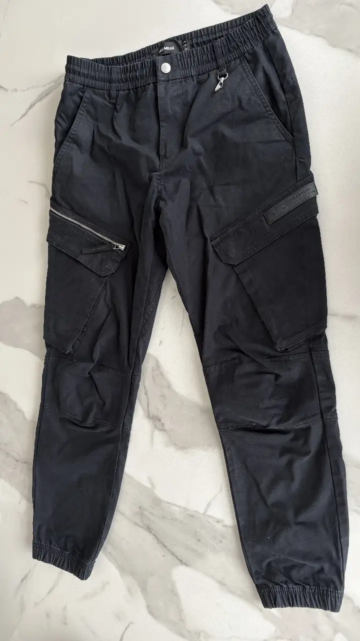 Pantalón cargo negro de niño, con bolsillos laterales y detalle de cierre en uno de ellos. Cintura elastizada con ajuste de cordón y detalle metálico. Ideal para un look urbano y funcional.
