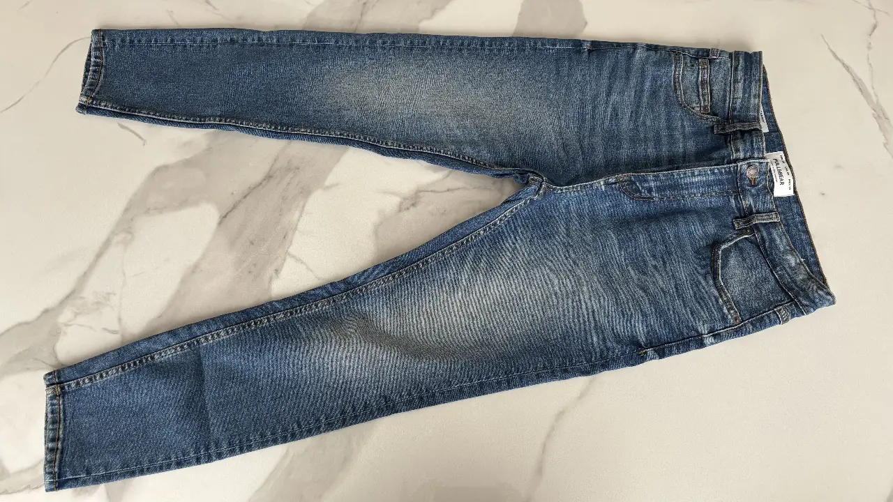 Jeans rectos de hombre, color azul gastado, con detalles de desgaste y etiqueta de la marca Pull&Bear. Talle 31.