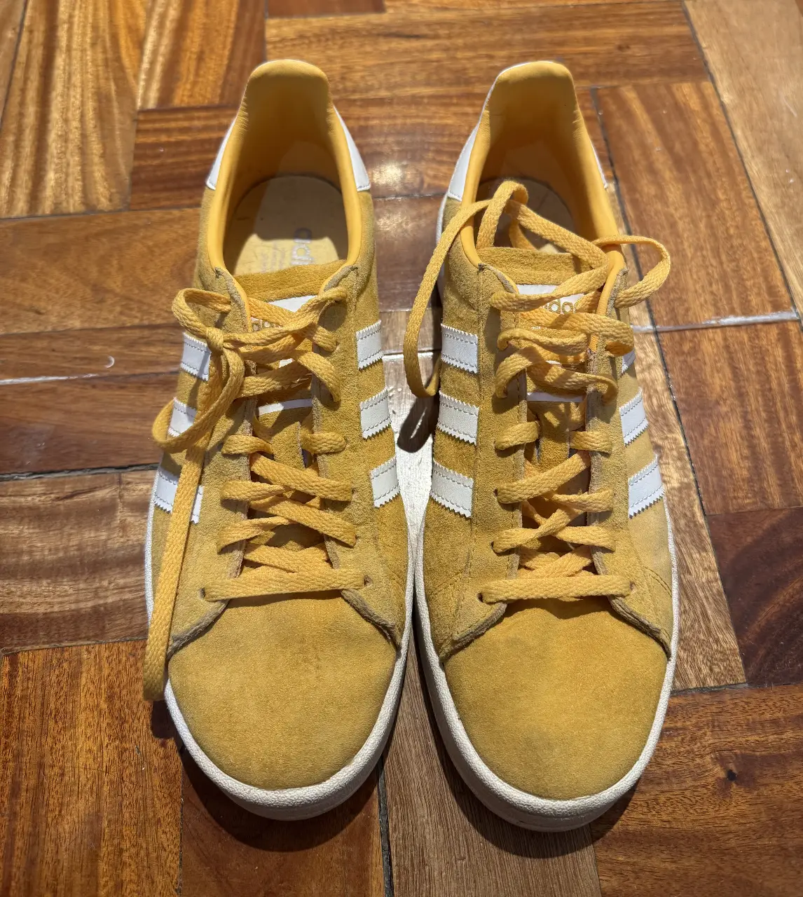 Zapatillas Adidas Campus amarillas con detalles blancos. Tienen las tres tiras características de la marca y la suela blanca. Ideales para un look casual y urbano.
