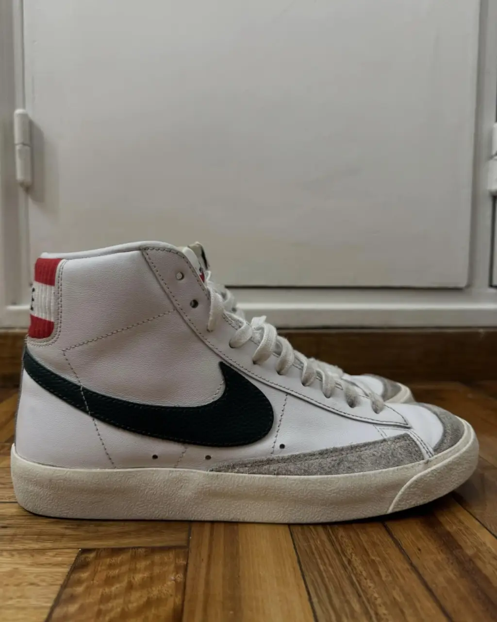 Zapatillas Nike Blazer Mid, blancas con el logo en verde oscuro y detalles en rojo y gris. Un clásico para un look casual y urbano.