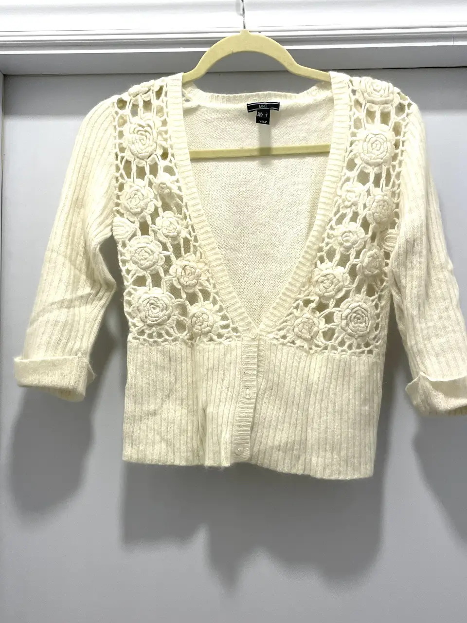 Cardigan de mujer color crudo con detalles de flores en crochet. Manga 3/4 y botones al frente. Ideal para un look casual y elegante.