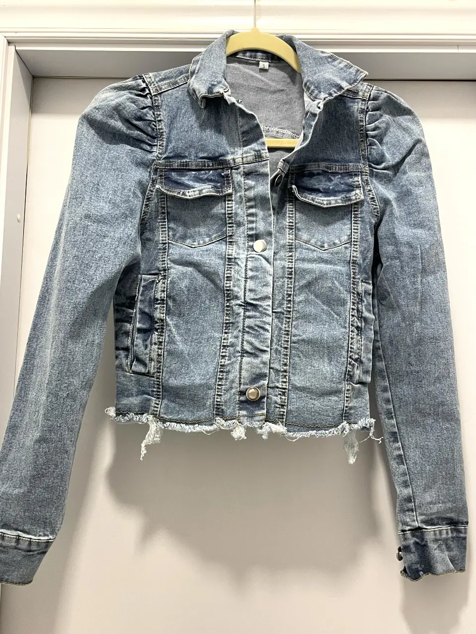 Campera de jean azul claro con detalles deshilachados en el bajo. Diseño con mangas abullonadas y dos bolsillos delanteros. Ideal para un look casual y moderno.