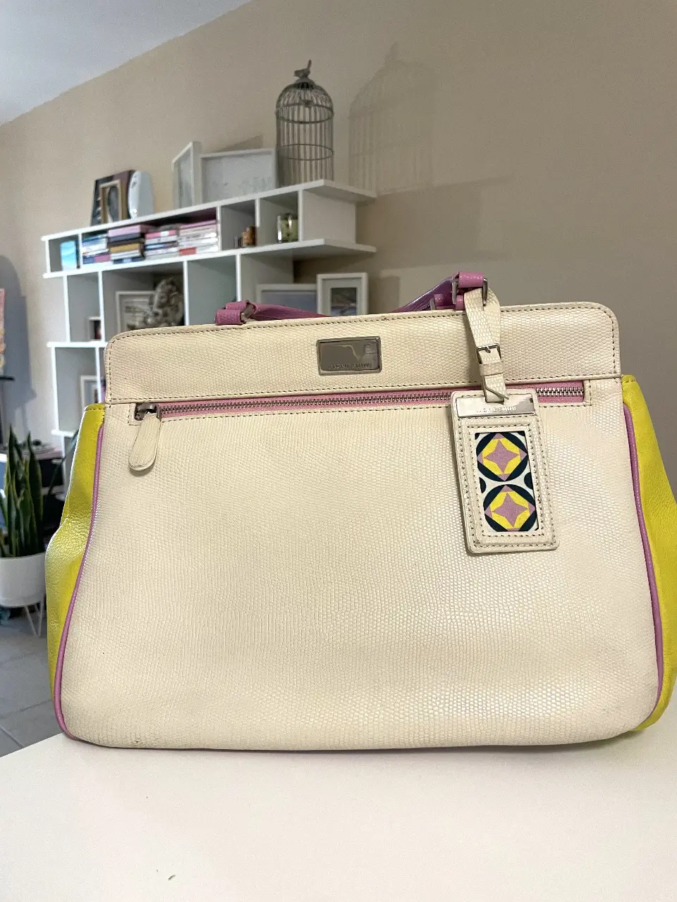 Cartera Jackie Smith de cuero, con detalles en amarillo y rosa. Posee un dije con diseño geométrico y cierre. Ideal para un look casual y elegante.
