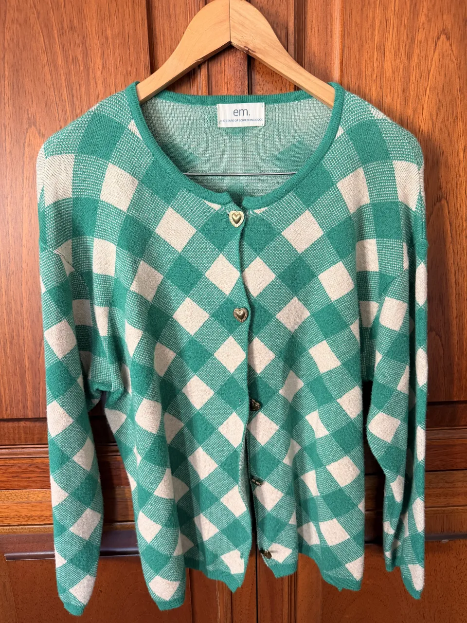 Cardigan a cuadros verdes y crudos con botones dorados en forma de corazón.