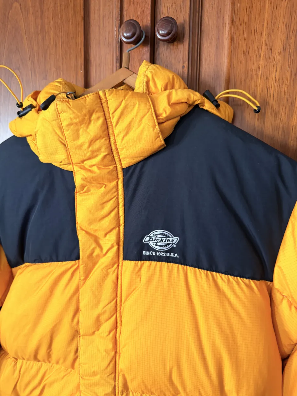 Campera puffer amarilla y negra con capucha. Tiene parches con el logo de la marca en la manga y en el interior. Cierre frontal y bolsillos con cierre. 100% pluma.