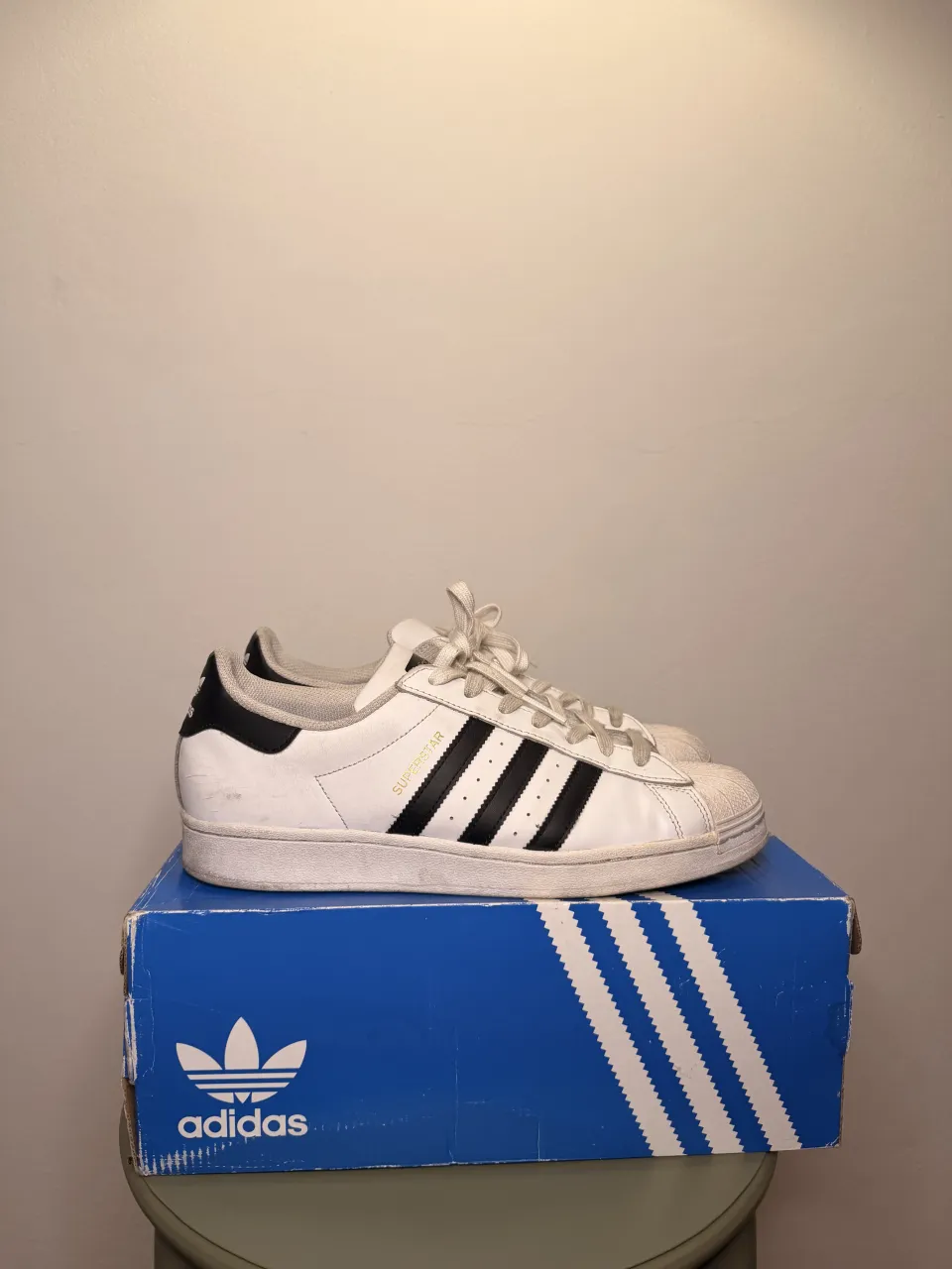 Zapatillas Adidas Superstar blancas con detalles negros. Tienen el logo de Adidas en la lengüeta y en el talón.
