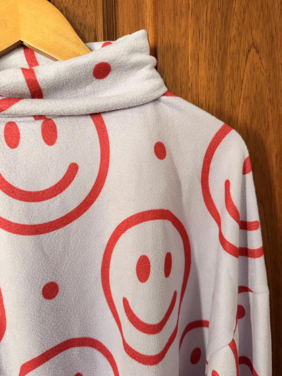 Buzo lila con cuello alto y estampa integral de caritas sonrientes rojas y puntos. Posee puños y cintura elastizados. Pilar.